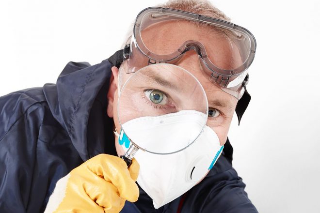 a pest control contractor or exterminator with a magnifying glass in his typical work dress at his work with chemicals against mold, pests bugs and other hygienic problems
